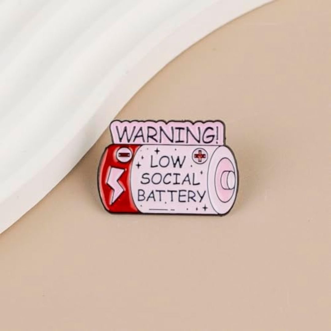 Low social battery enamel pin with pink battery design, red details and warning message.