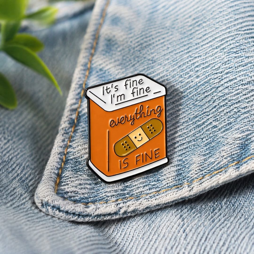 It's Fine enamel pin featuring an orange tin can, bandage illustration and humorous lettering.