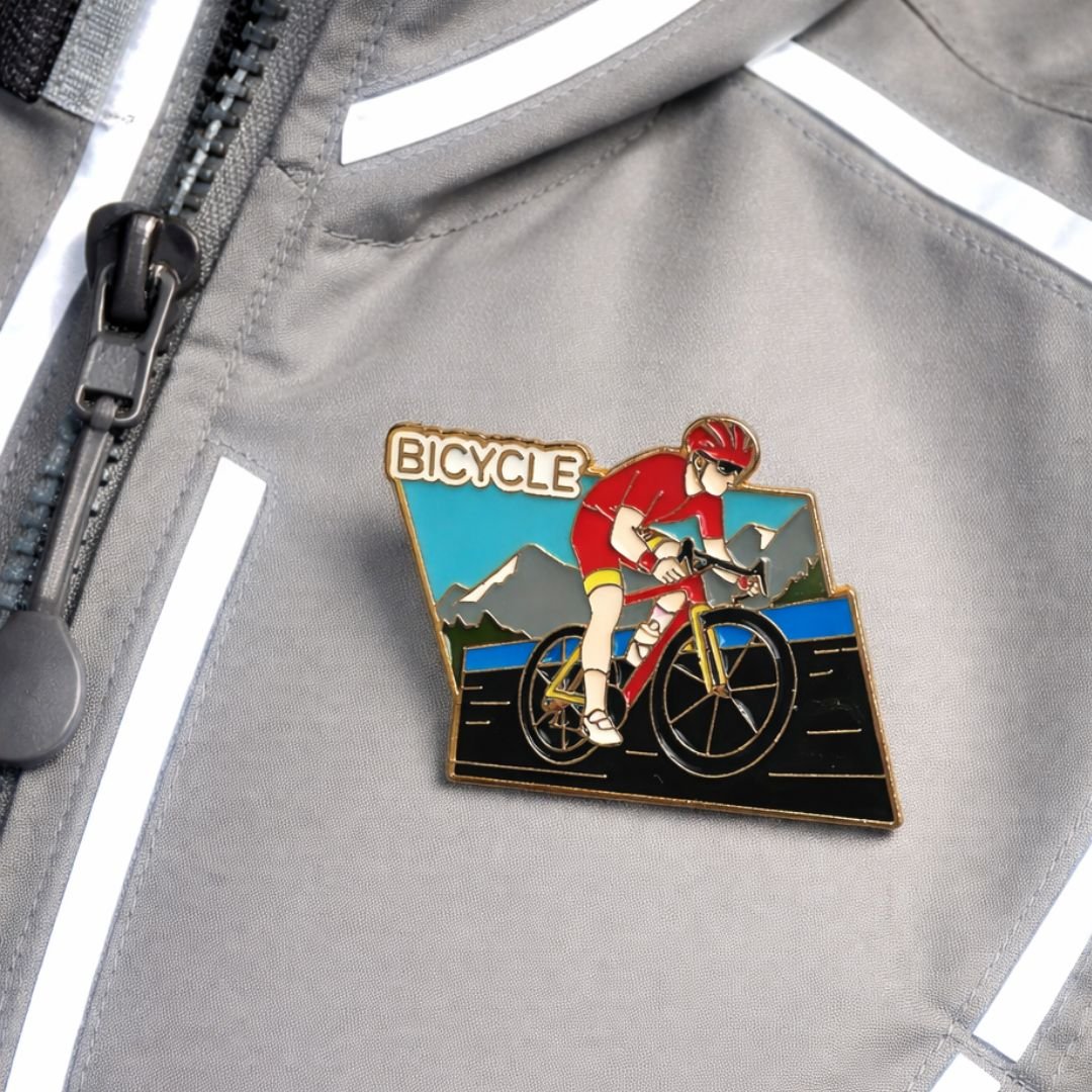 Bicycle enamel pin featuring a cyclist riding against a colourful mountain and road backdrop.