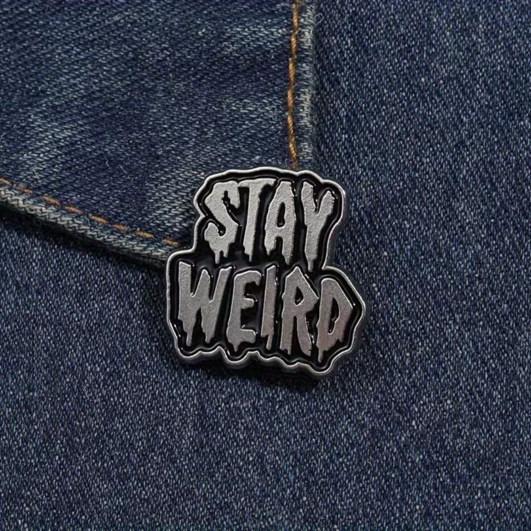 Stay Weird enamel pin featuring bold black-and-white lettering with an irregular outline.