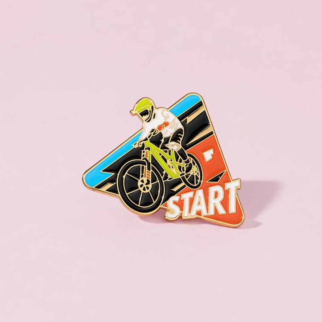 Cycle Start enamel pin featuring a cyclist on a bicycle with colourful racing graphics.